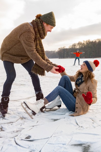 Man helping ice skating woman up on icy surface of frozen lake, Cologne, NRW, Germany